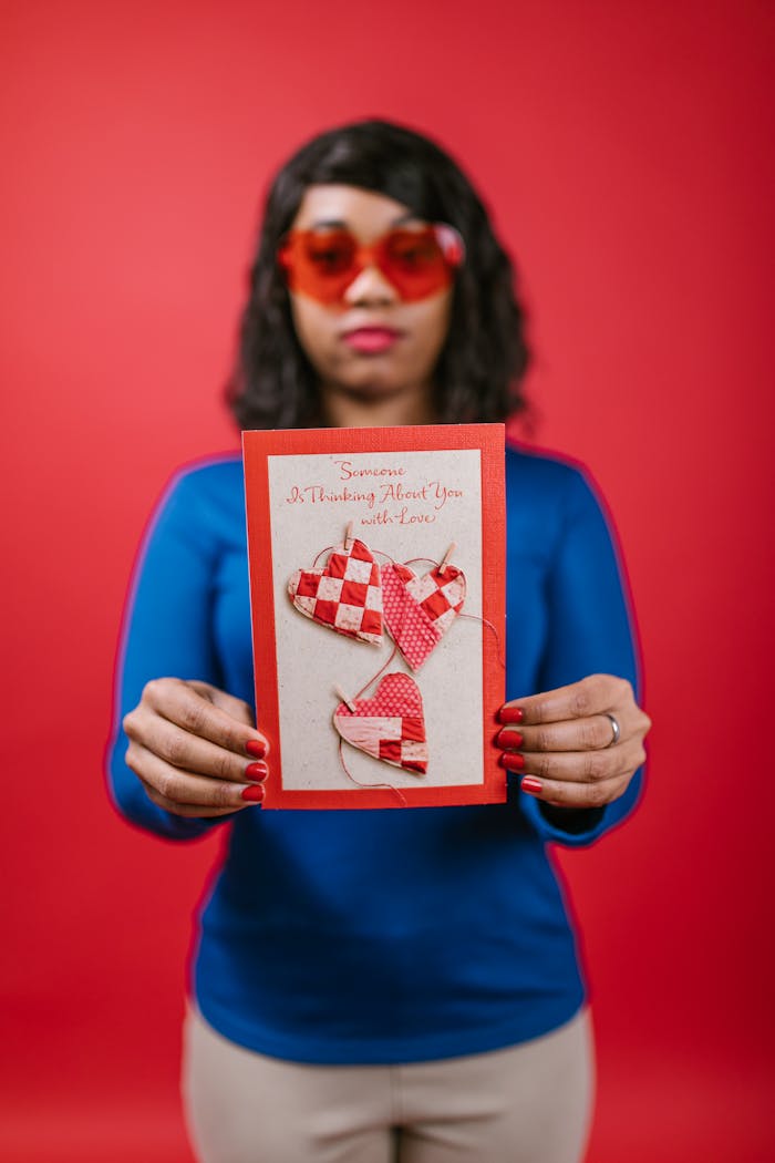 A woman wearing red heart-shaped glasses holds a Valentine's card featuring red and white hearts.